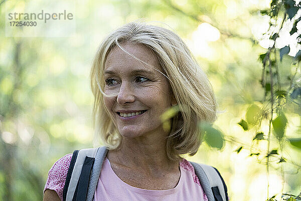 Porträt einer lächelnden reifen Frau mit Rucksack im Wald