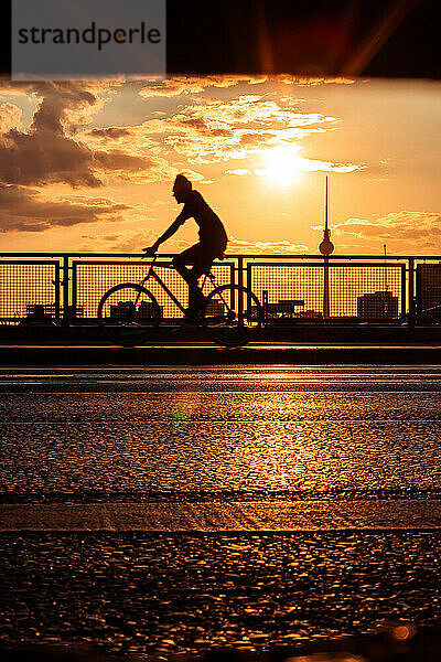 Silhouette eines Mannes auf einer Brücke mit Fernsehturm Berlin im Hintergrund bei Sonnenuntergang