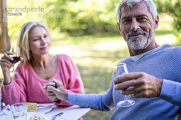 Porträt eines reifen Mannes  der die Hand seiner Frau hält und im Hinterhof Rotwein trinkt