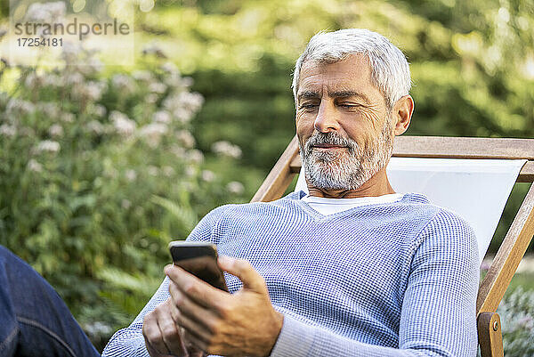 Lächelnder reifer Mann  der ein Smartphone benutzt  während er auf einem Liegestuhl sitzt