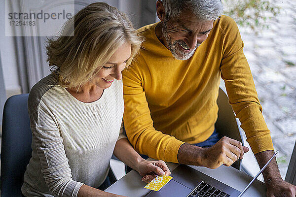 Erhöhte Ansicht eines lächelnden reifen Paares bei der Online-Zahlung mit Kreditkarte