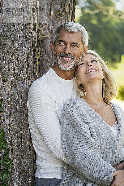 Lächelndes reifes Paar lehnt sich an einen Baumstamm