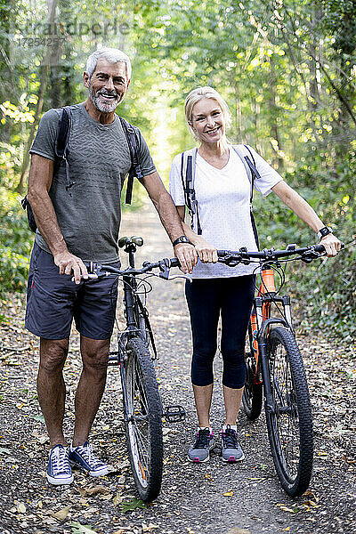 Porträt eines lächelnden reifen Paares mit Fahrrädern auf einem Fußweg im Wald