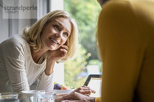 Lächelnde reife Frau sieht ihren Mann an  während sie ein digitales Tablet benutzt