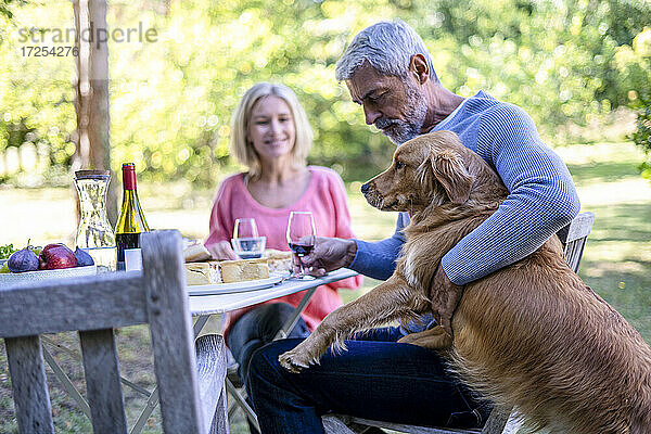 Älterer Mann hält Weinglas und spielt mit Hund im Hinterhof