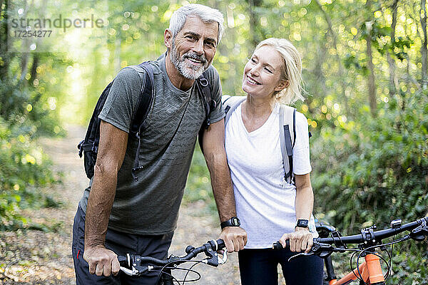 Lächelndes reifes Paar mit Fahrrädern im Wald stehend