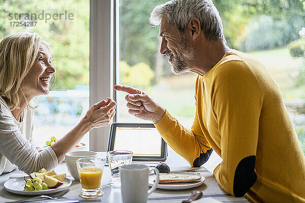 Lächelndes reifes Paar  das beim Frühstück miteinander spricht