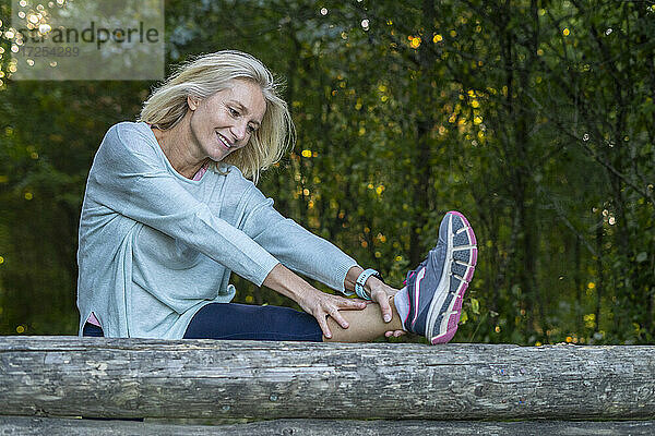 Lächelnde reife Frau streckt ihr Bein im Wald