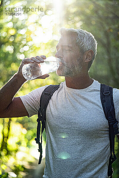 Älterer Mann trinkt Wasser im Wald an einem sonnigen Tag
