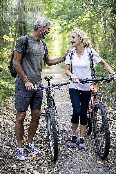 Lächelndes reifes Paar mit Fahrrädern auf einem Fußweg im Wald