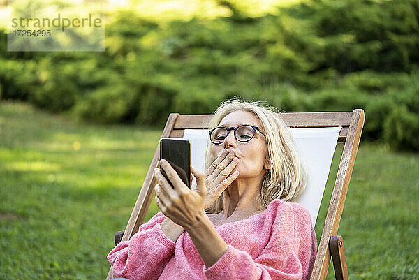 Lächelnde reife Frau  die sich einen Kuss zuwirft  während sie einen Videoanruf auf einem Smartphone führt