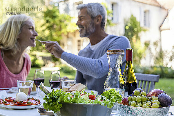 Lächelnder reifer Mann  der seine Frau füttert  mit Essen auf dem Tisch im Vordergrund
