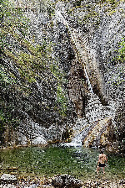 Frankreich  Alpes-de-Haute-Provence  Mann in Teich mit Blick auf Wasserfall auf erodiertem Fels