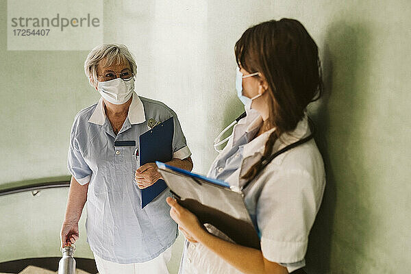 Weibliches Gesundheitspersonal mit Gesichtsmaske bei der Diskussion in einer medizinischen Klinik während COVID-19