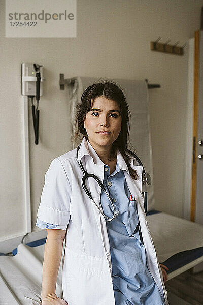 Porträt einer weiblichen medizinischen Fachkraft  die sich auf einen Untersuchungstisch in einer medizinischen Klinik stützt