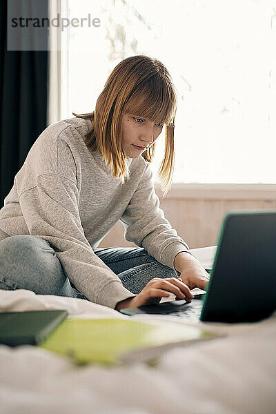 Teenager-Mädchen tippt auf dem Laptop  während er Hausaufgaben zu Hause