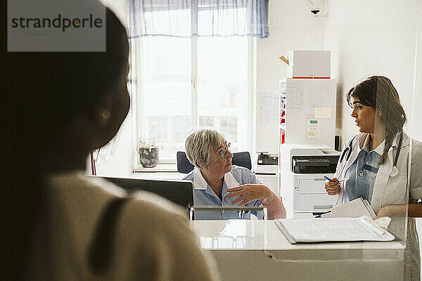 Ältere weibliche Krankenschwester diskutiert mit Arzt durch Glas in der medizinischen Klinik gesehen