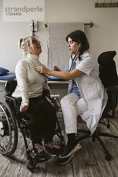 Volle Länge der weiblichen Gesundheitspflegekraft  die einen behinderten Patienten mit Stethoskop in einer medizinischen Klinik untersucht