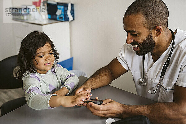 Lächelnder männlicher Kinderarzt  der den Zuckerspiegel eines Mädchens in einer medizinischen Klinik überprüft