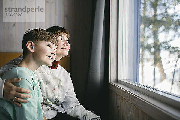 Glückliche Mutter und Sohn sitzen zusammen und schauen durch das Fenster