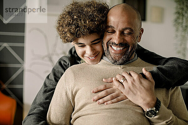 Porträt eines lächelnden Jungen  der seinen fröhlichen Vater von hinten umarmt