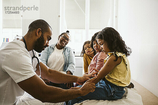 Mutter und Töchter schauen auf den männlichen Arzt  der die Hand des Mädchens in der medizinischen Klinik untersucht