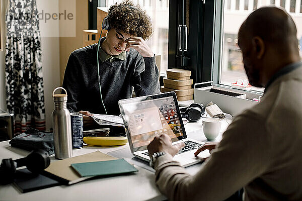 Junge trägt Kopfhörer studieren  während mit Geschäftsmann mit Laptop am Schreibtisch sitzen