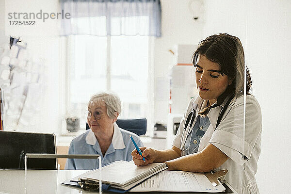 Weibliche Gesundheitspflegekraft schreibt ein Rezept  während sie neben einer älteren Krankenschwester steht
