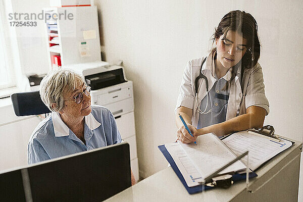 Senior weibliche Krankenschwester Blick auf Arzt schreiben Rezept in der medizinischen Klinik