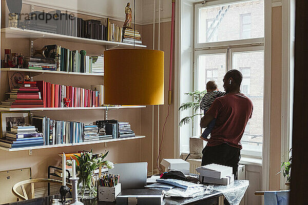 Männlicher Unternehmer trägt Kleinkind im Stehen im Home Office