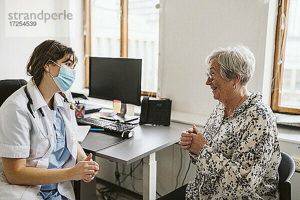 Lächelnde ältere Patientin im Gespräch mit einem medizinischen Experten mit Gesichtsmaske