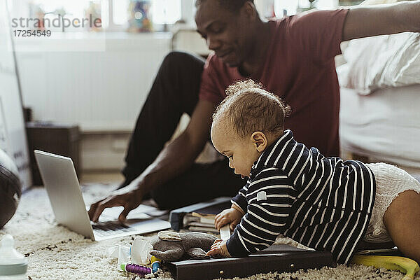 Männliches Kleinkind spielt mit Spielzeug von Vater mit Laptop im Schlafzimmer