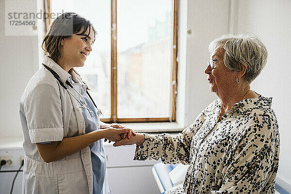 Lächelnde weibliche Gesundheitspersonal Blick auf ältere Patienten im Gespräch  während die Hände halten