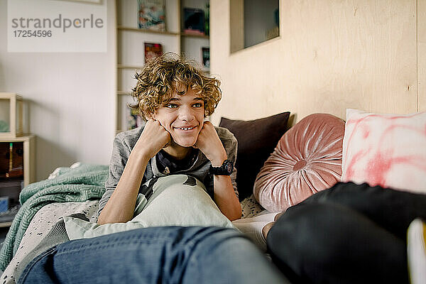 Lächelnder Junge mit braunen Haaren liegt auf dem Bett zu Hause