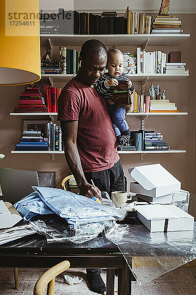 Männlicher Unternehmer schreibt  während er einen kleinen Jungen zu Hause trägt