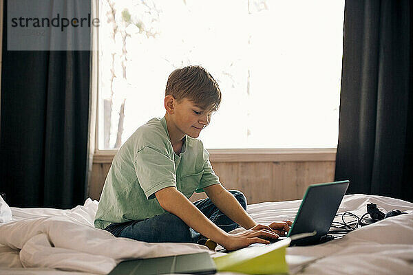 Junge mit Laptop bei den Hausaufgaben im Schlafzimmer