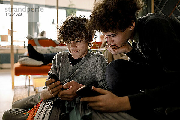 Jungen teilen Mobiltelefon beim Sitzen im Wohnzimmer