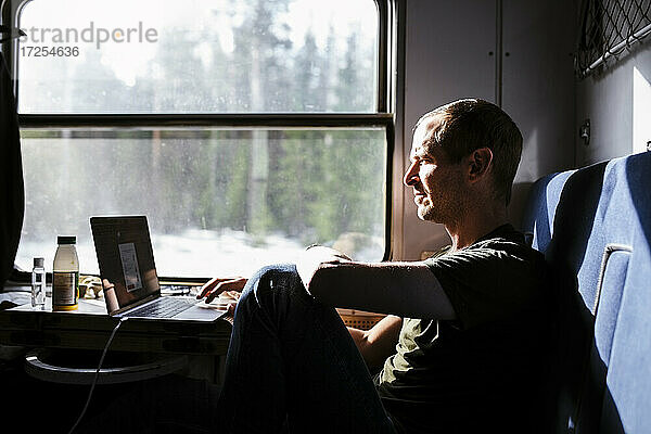 Geschäftsmann mit Laptop beim Sitzen am Fenster im Zug