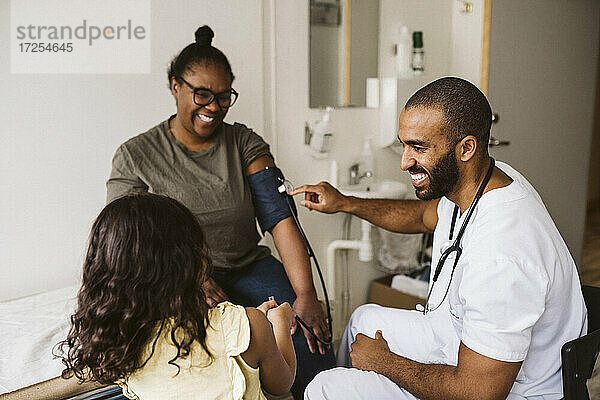 Lachend männlichen Gesundheitswesen Arbeiter Blick auf Mädchen während der Messung Frau Blutdruck in der medizinischen Klinik