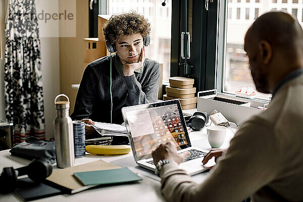 Teenager Junge schaut auf männlichen Unternehmer arbeiten  während am Schreibtisch sitzen
