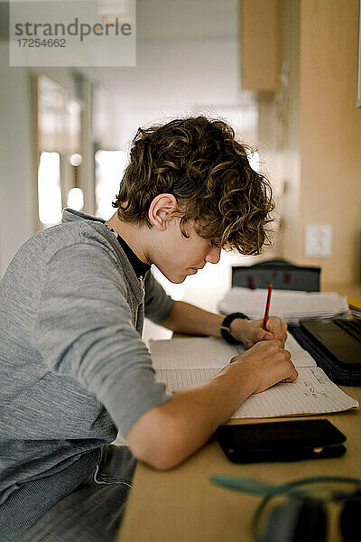 Junge schreibt in Buch  während er am Tisch sitzend Hausaufgaben macht