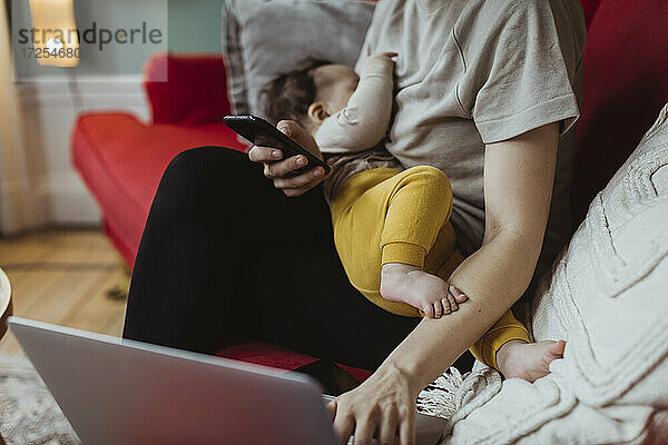 Midsection von Geschäftsfrau mit Baby Junge arbeiten am Laptop im Büro zu Hause