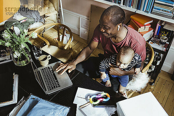 Lächelnde Geschäftsmann mit Laptop  während mit männlichen Kleinkind im Büro zu Hause sitzen