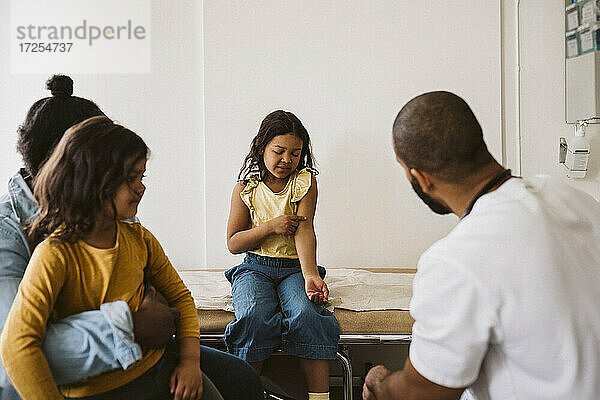 Mädchen im Gespräch mit männlichen Arzt  während er auf die Hand in der medizinischen Klinik zeigt