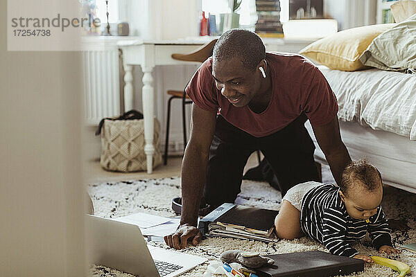Lächelnde Papa-Unternehmer Blick auf Laptop  während kniend hinter Sohn im Schlafzimmer
