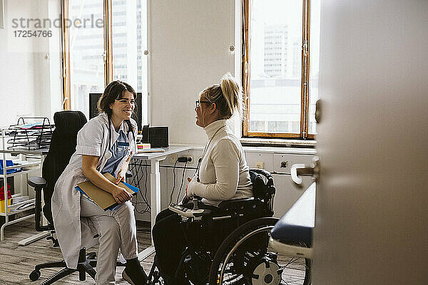 Lächelnder weiblicher medizinischer Experte  der eine behinderte Frau im Gespräch in einer medizinischen Klinik betrachtet