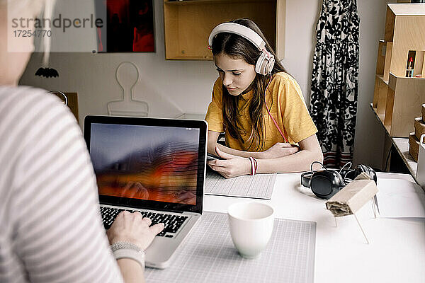 Mädchen mit Kopfhörer E-Learning durch digitale Tablette  während sie mit Geschäftsfrau arbeiten auf Laptop am Schreibtisch sitzen
