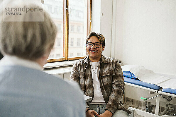 Lächelnde junge männliche Patient Blick auf ältere weibliche Arzt in der medizinischen Klinik