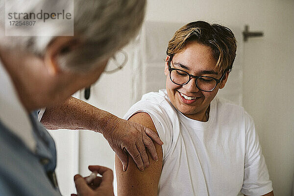 Lächelnd jungen männlichen Patienten Blick auf ältere weibliche medizinische Experten geben Impfstoff