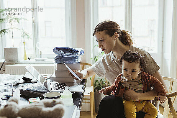 Geschäftsfrau liest Dokument  während sie mit Baby Junge im Wohnzimmer sitzt